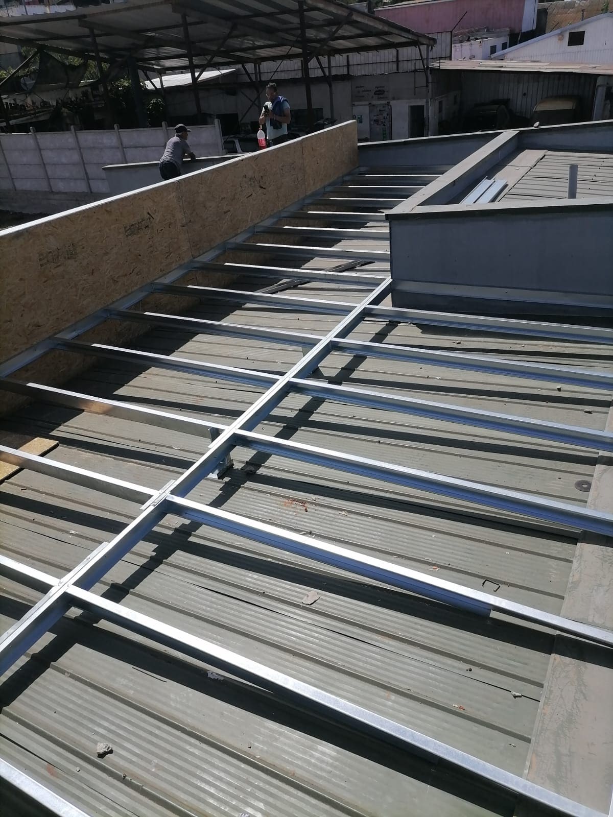 Maestros trabajando en estructura de techumbre metálica sobre edificio industrial